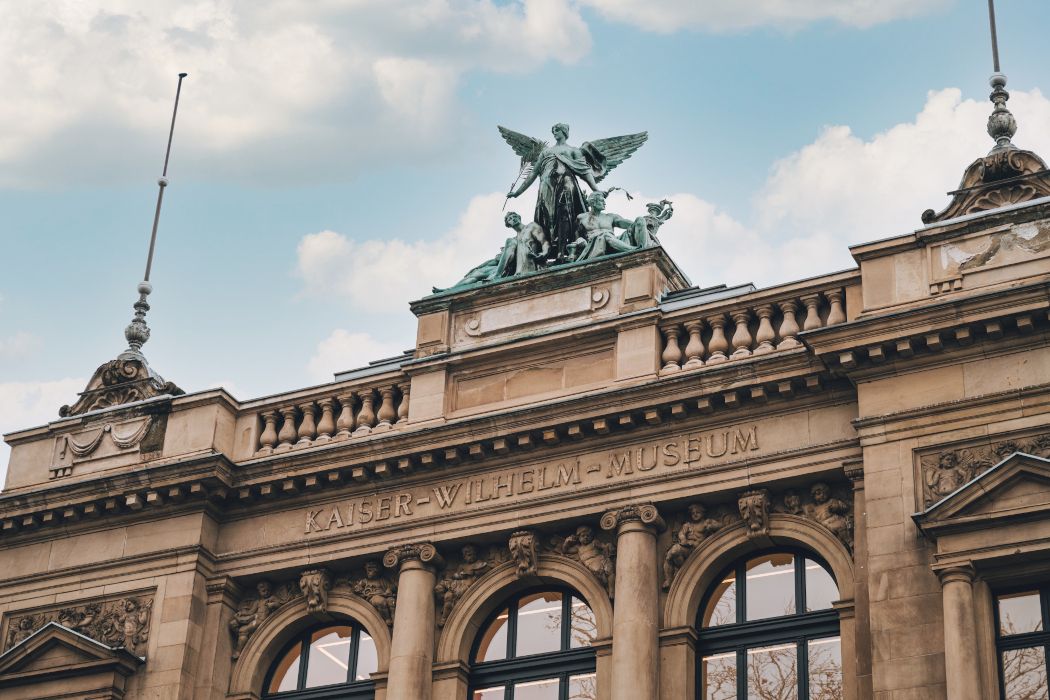 Het Kaiser Wilhelm Museum is versierd met de 1,7 ton zware bronzen groep Genius der Künste.