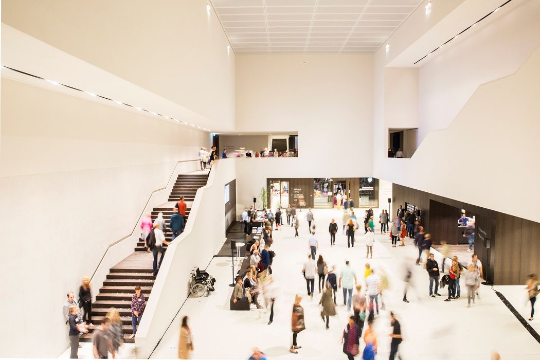 Gasten lopen rond in de met licht overgoten foyer van het museum