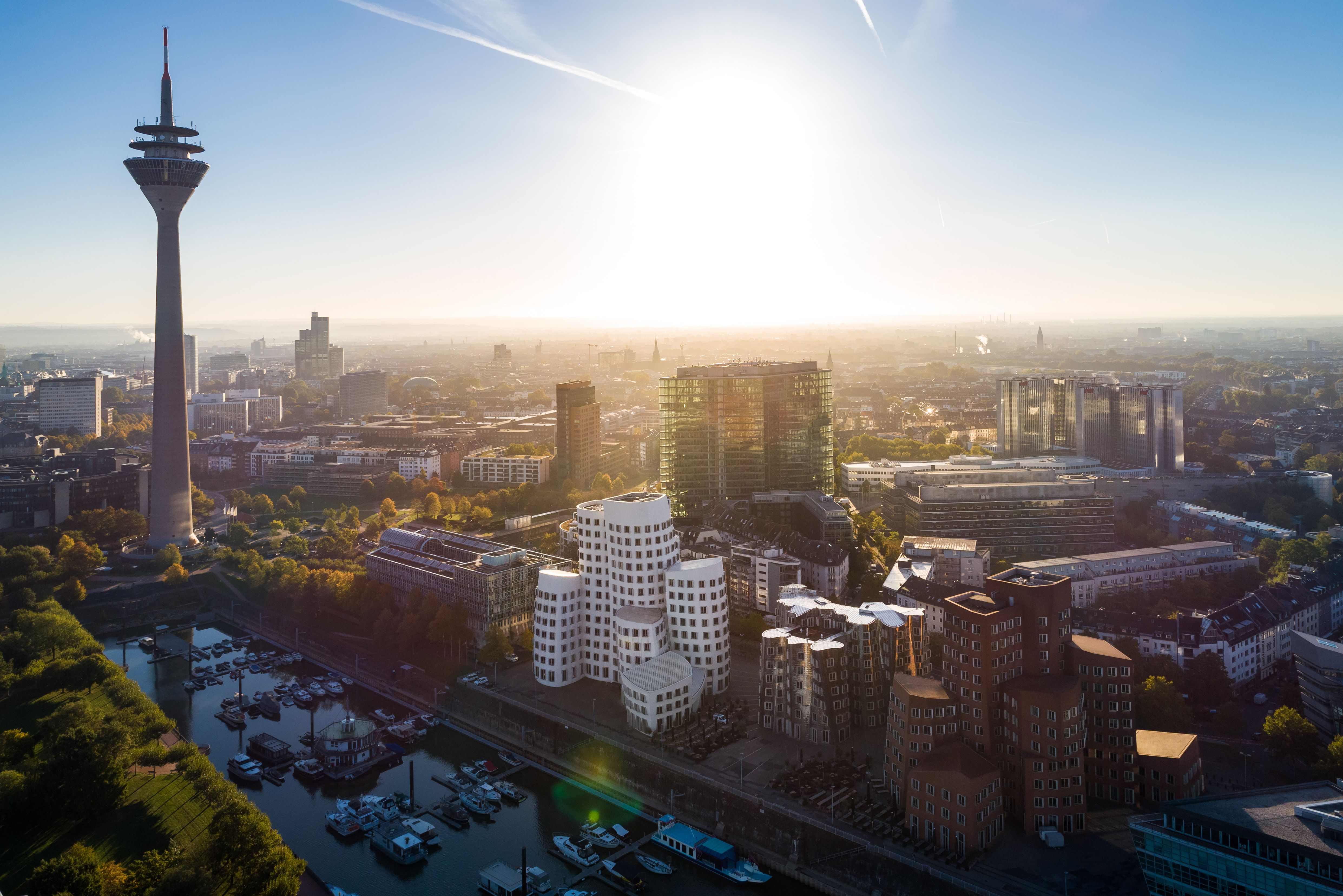 Sonne steht am Himmel über Düsseldorf, im Vordergrund sind Hafenbecken, Gehry-Bauten und Fernsehtum zu sehen